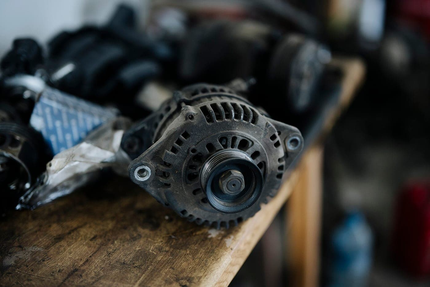 Car alternator on a workbench surrounded by various auto parts in a garage setting